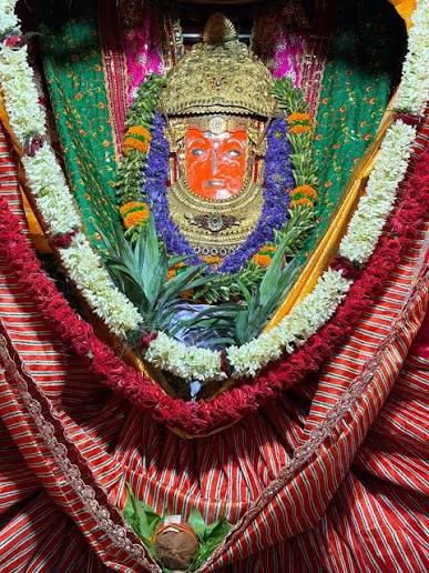 Morning shringar of Jeen Mata with golden crown, purple and white flower garlands, green leaves and red striped poshak